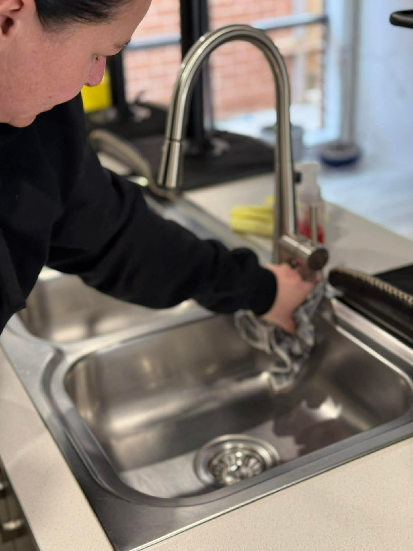 No.1 Cleaning team member deep cleaning a stainless steel kitchen sink and tap
