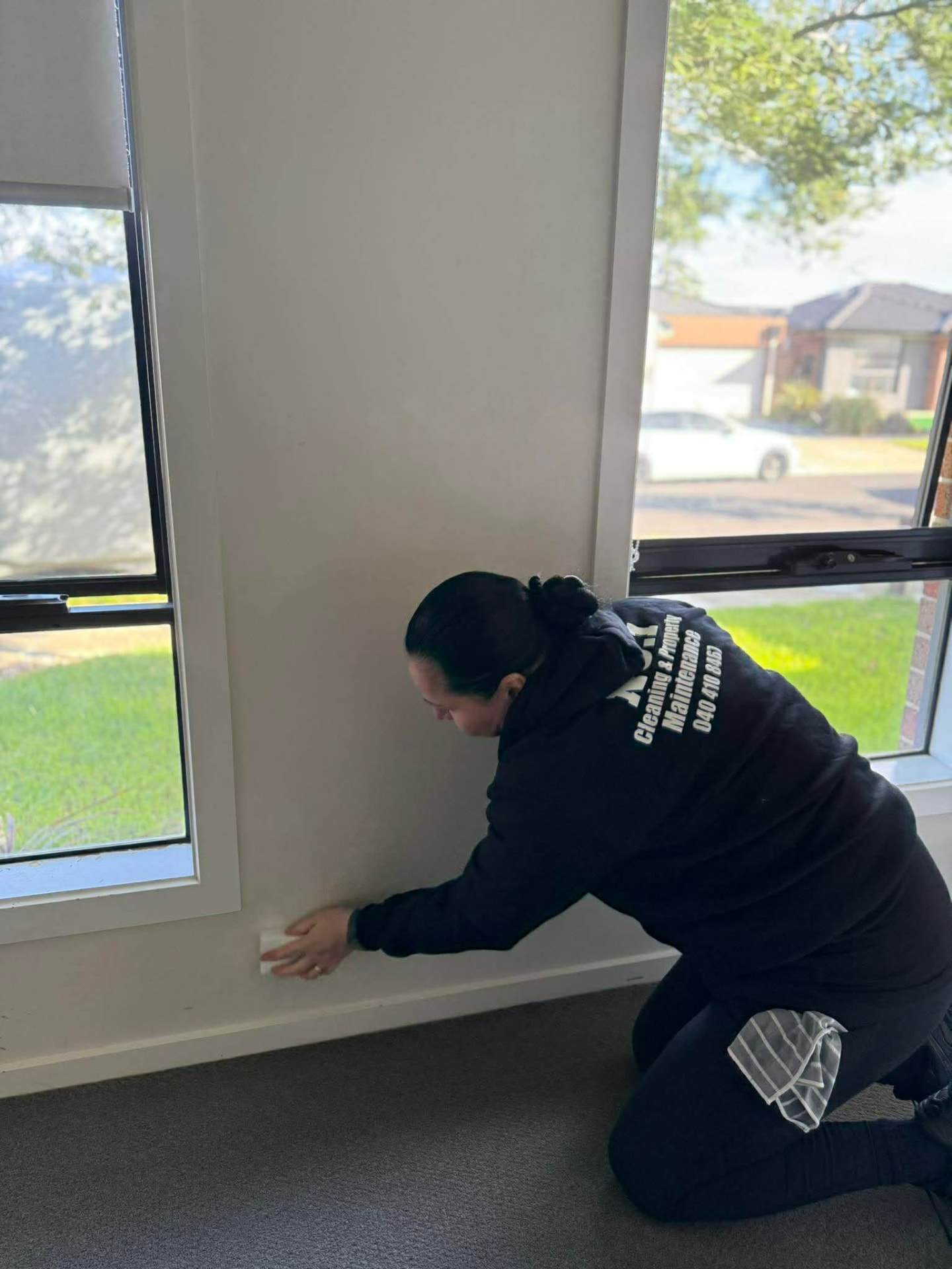 A No.1 Cleaning team member wiping down skirting boards by a window